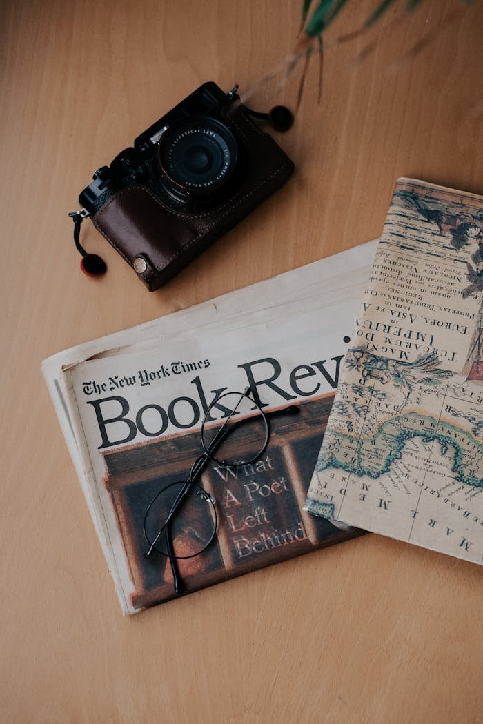 Flat lay of vintage camera, map, and book review on wooden surface.